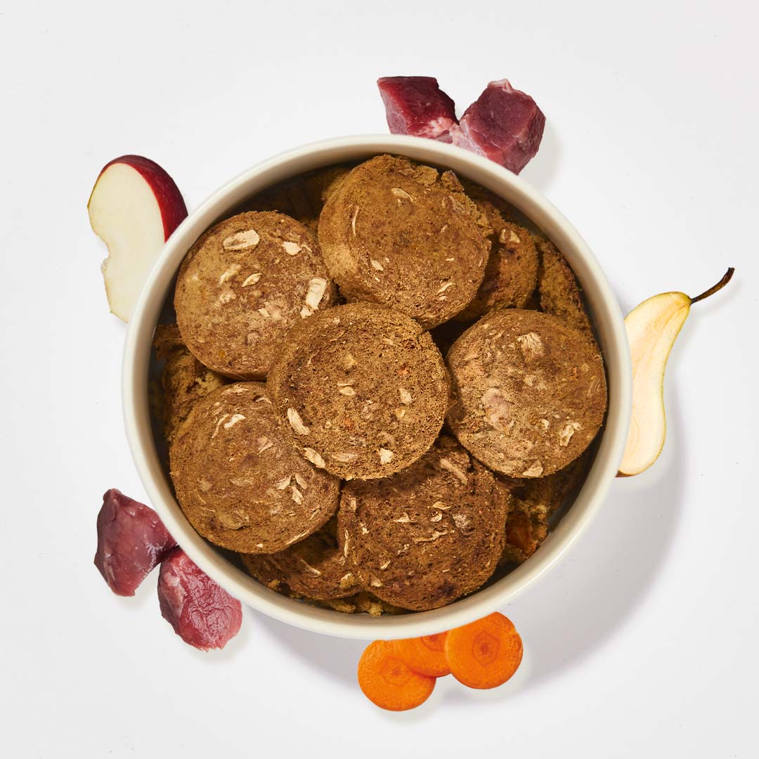 Gefriergetrocknete BARF2GO Komfort Plus Lamm Taler für Hunde in Schüssel mit Apfel, Karotte, Birne und Lammfleisch Stücken auf weißem Hintergrund